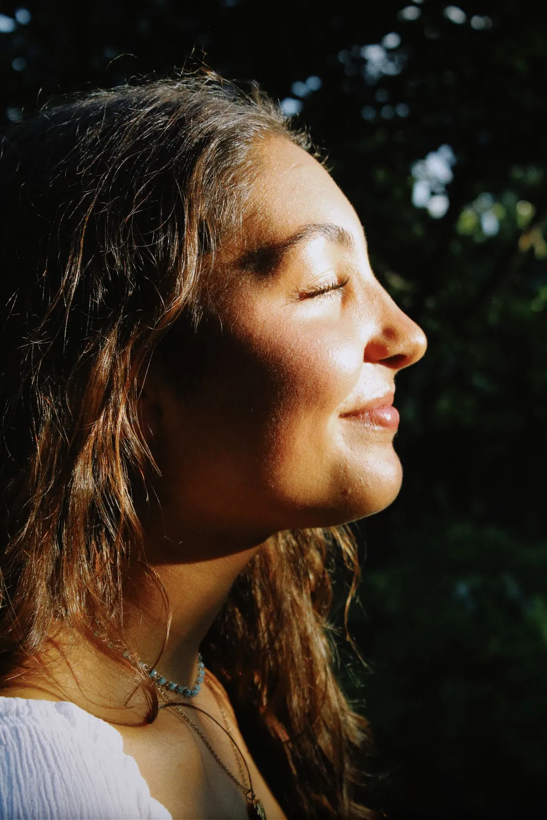 A woman with her eyes closed, smiling in warm sunlight
