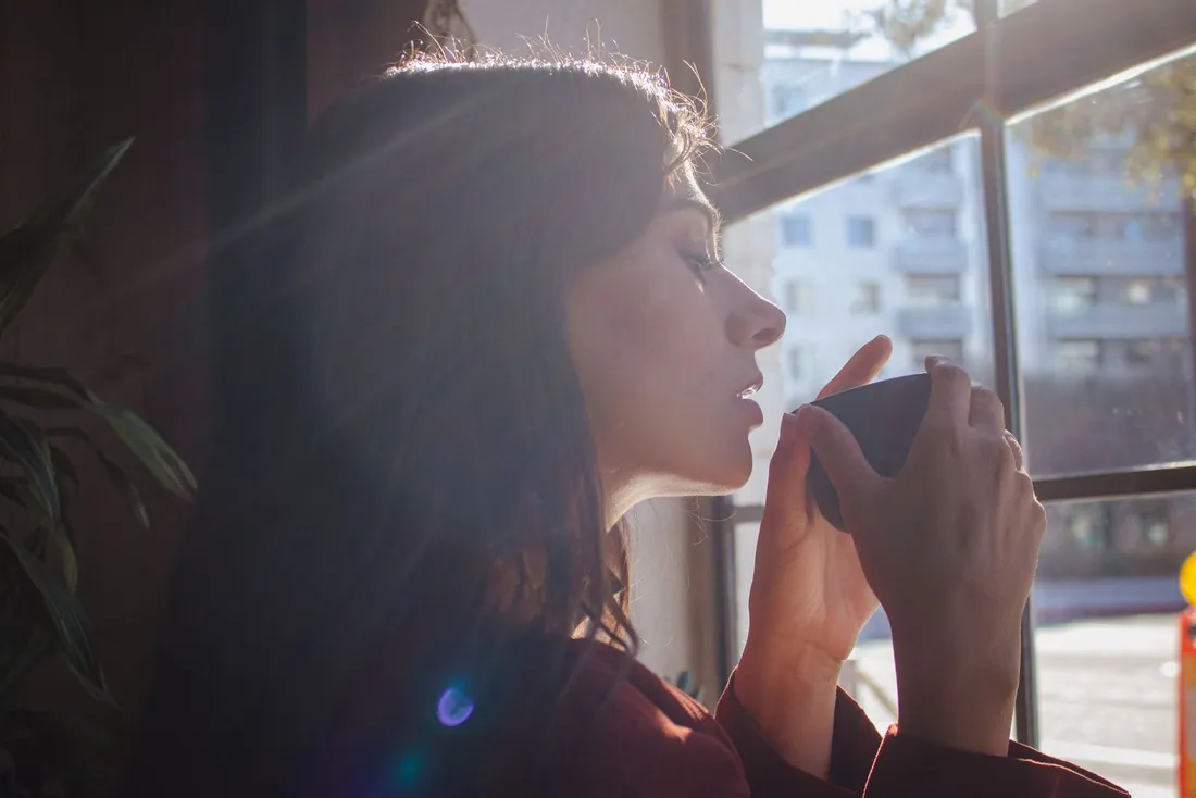 A woman holding a warm drink by a sunlit window