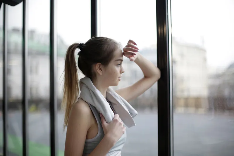 A woman in athletic wear with a towel over her shoulders by a window