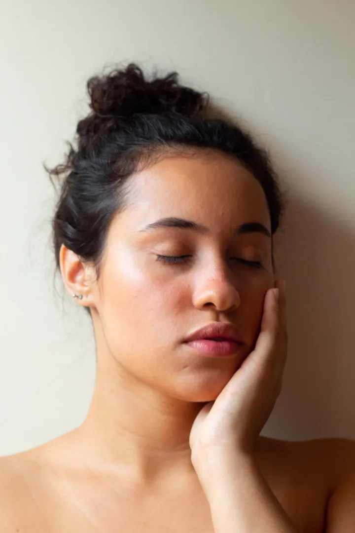 A woman with her eyes closed and a hand resting on her cheek